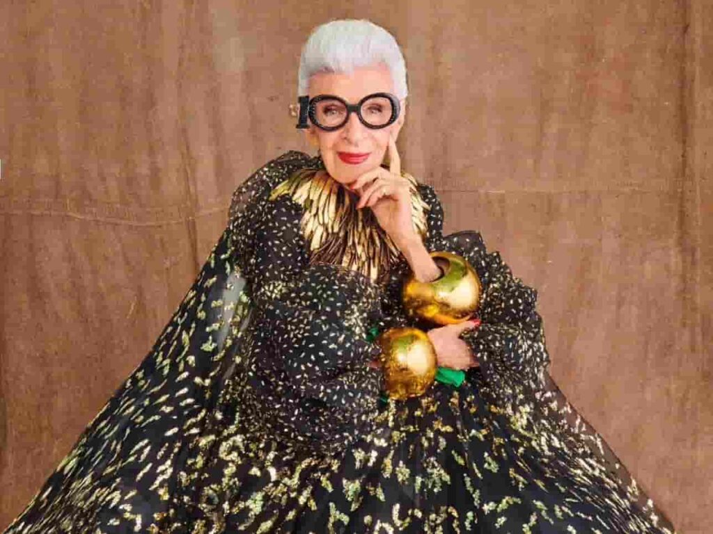 Iris Apfel wearing her signature glasses and colorful attire.